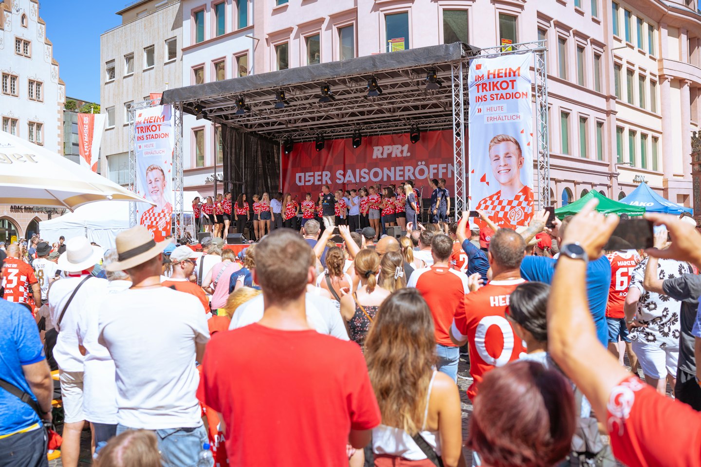 Publik som ser på artister på en scen på ett stads torg.